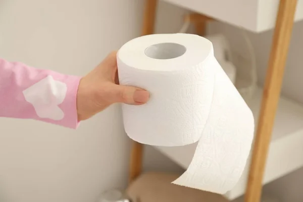 Młoda kobieta trzyma miękkie papier toaletowy z półki w toalecie — Zdjęcie stockowe