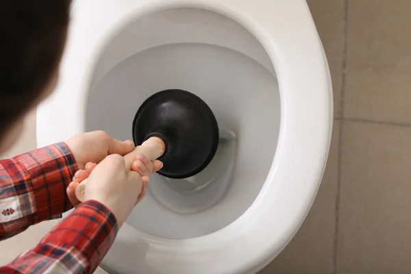 Ung kvinna som använder kolven för att rensa en toalett skål — Stockfoto