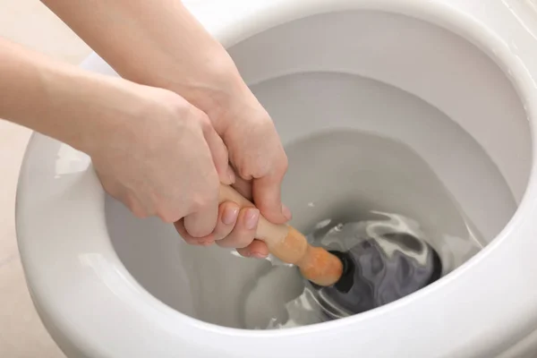 Young woman using plunger to unclog a toilet bowl — Stock Photo, Image