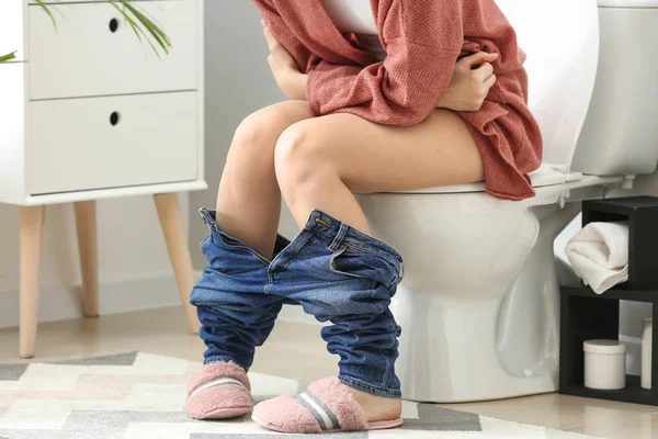 Young woman sitting on toilet bowl in restroom — Stock Photo, Image