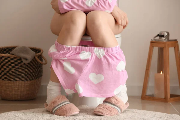 Jeune femme assise sur la cuvette des toilettes dans les toilettes — Photo