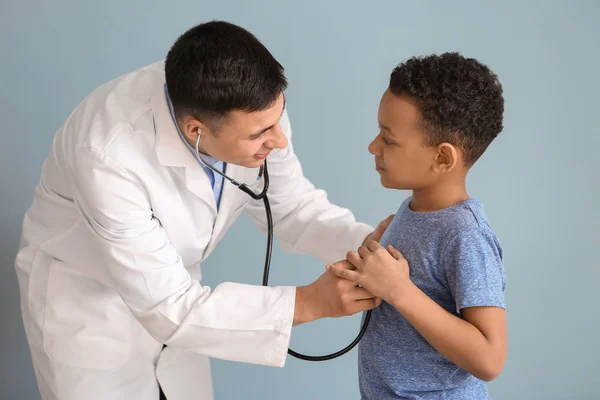 Pediatra examinando menino afro-americano em fundo de cor — Fotografia de Stock
