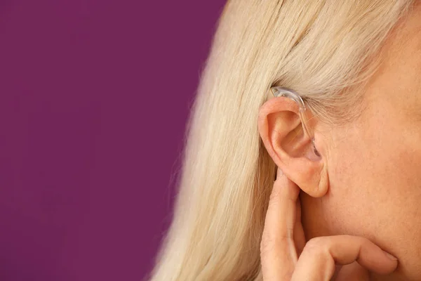 Oudere vrouw met gehoorapparaat op kleur achtergrond, close-up — Stockfoto