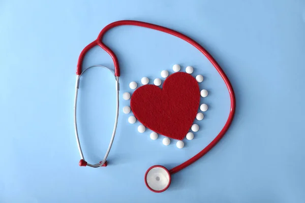 Estetoscópio com coração e pílulas em fundo de cor — Fotografia de Stock