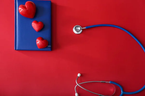 Stethoscope with notebook and hearts on color background — Stock Photo, Image