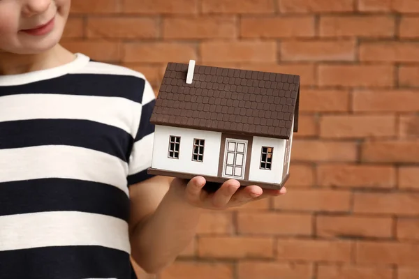 Little boy with model of house on brick background, closeup. Concept of earthquake