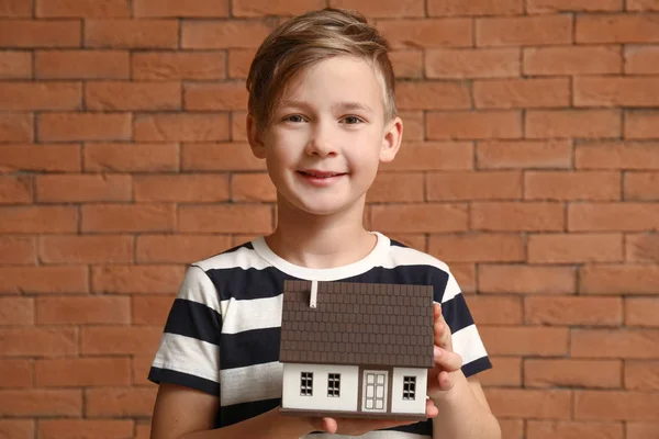 Little boy with model of house on brick background. Concept of earthquake — Stock Photo, Image