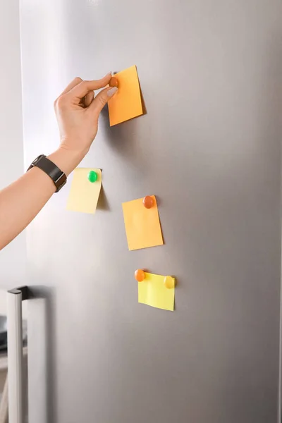 Žena připevňování papírů ke dveřím ledničky — Stock fotografie