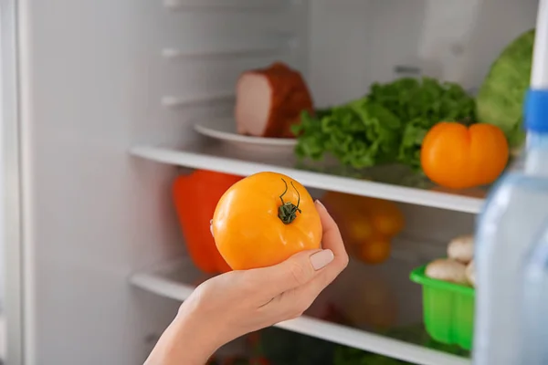 Frau holt Tomate aus Kühlschrank — Stockfoto