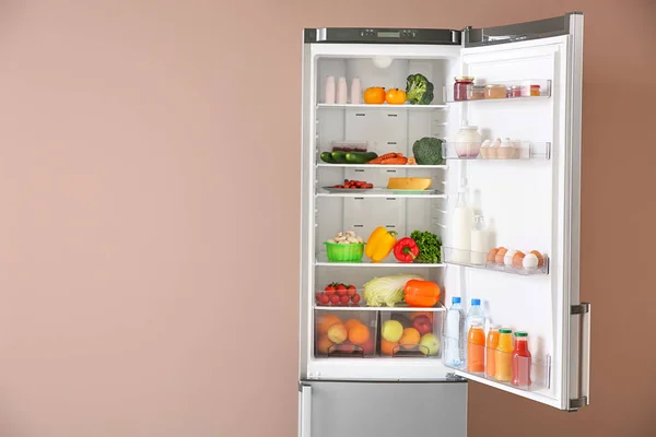 Otevřená lednička plná jídla v blízkosti barevné zdi — Stock fotografie
