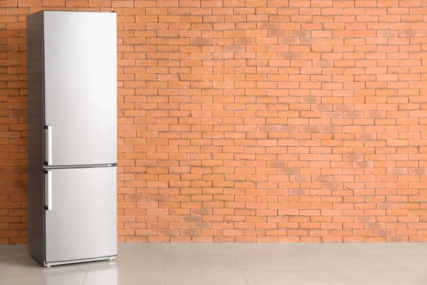 Modern fridge near brick wall