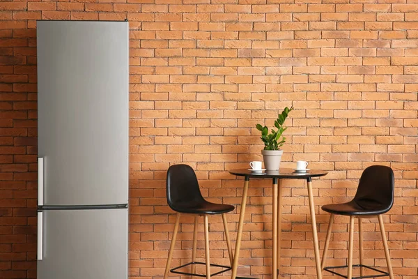 Modern fridge, table and chairs in kitchen — Stock Photo, Image