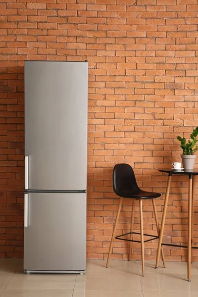 Modern fridge, table and chair in kitchen — Stock Photo, Image