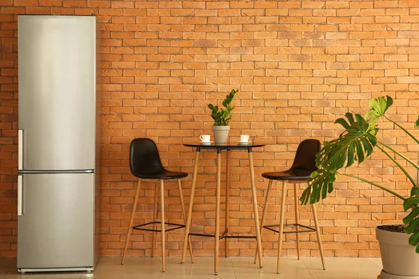 Modern fridge, table and chairs in kitchen — Stock Photo, Image