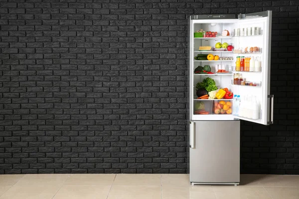 Offener Kühlschrank voller Lebensmittel in der Nähe dunkler Ziegelwände — Stockfoto