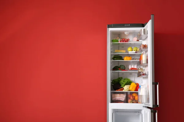 Open fridge full of food near color wall — Stock Photo, Image