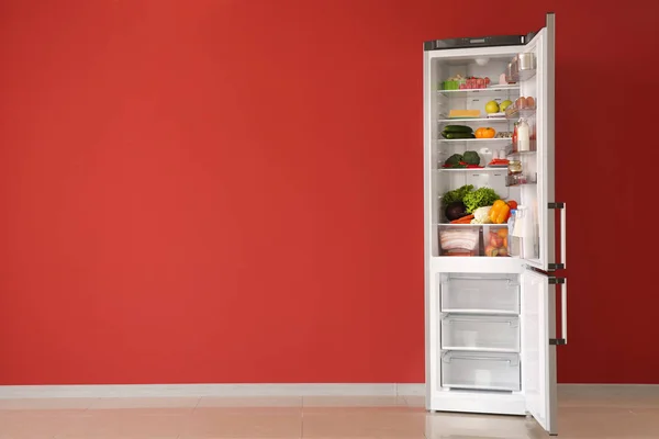 Nevera abierta llena de comida cerca de la pared de color — Foto de Stock