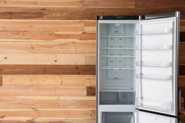 Open empty fridge near wooden wall — Stock Photo, Image