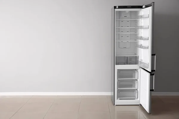 Open empty fridge near light wall — Stock Photo, Image