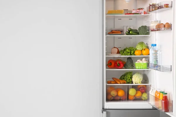 Offener Kühlschrank voller Lebensmittel in der Nähe der weißen Wand — Stockfoto