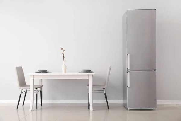 Modern fridge and served table in kitchen — Stock Photo, Image