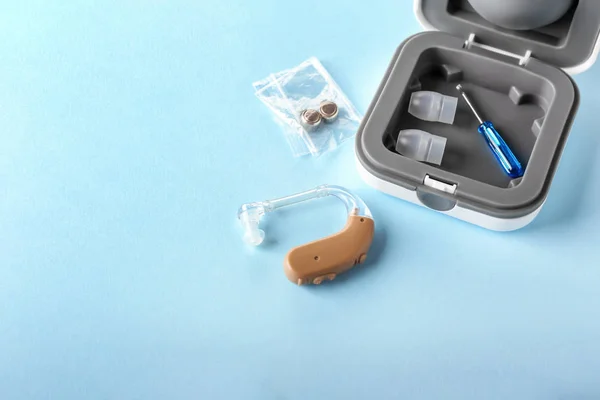 Box with hearing aid and accessories on color background