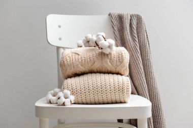 Gri arka plana karşı beyaz sandalyede pamuklu çiçekler ile örme kazak