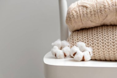 Gri arka plana karşı beyaz sandalyede pamuklu çiçekler ile örme kazak
