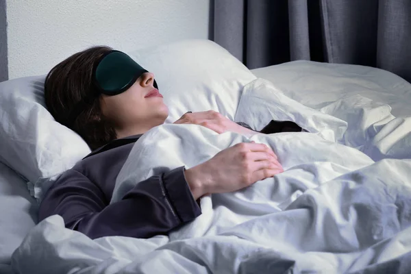 Jovem com máscara de sono na cama à noite — Fotografia de Stock