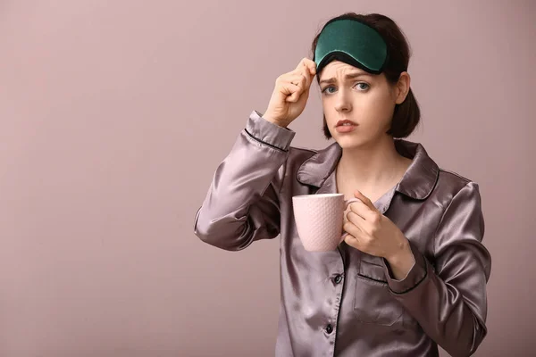 Sad woman with sleep mask and cup of coffee on color background — Stock Photo, Image