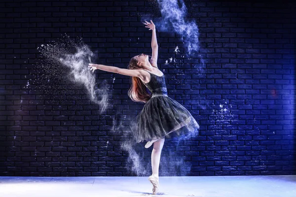 Mooie jonge ballerina dansen met poeder tegen donkere muur — Stockfoto