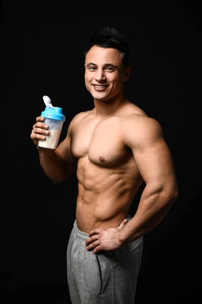 Sportlicher Mann mit Proteinshake auf dunklem Hintergrund — Stockfoto