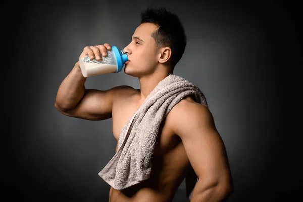 Sporty man drinking protein shake on dark background