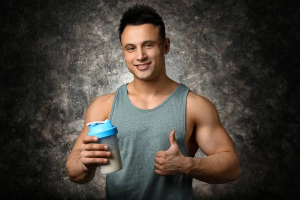 Sporty man with protein shake on dark background