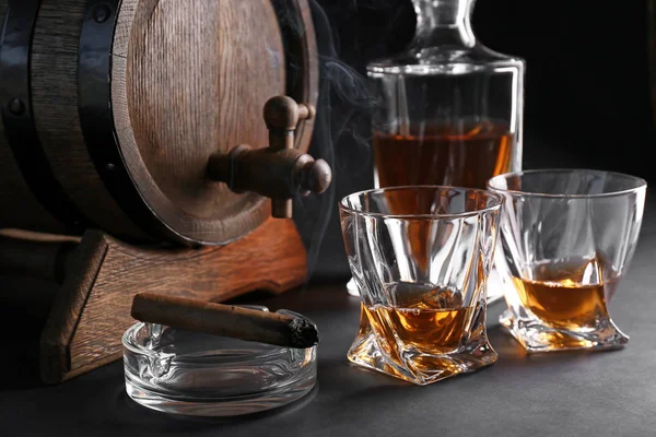 Glasses of cold whiskey with cigar and barrel on dark background — Stock Photo, Image