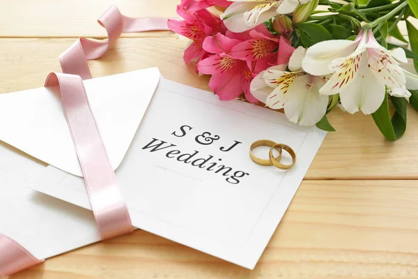 Zaproszenia ślubne, obrączki i kwiaty na stole — Zdjęcie stockowe