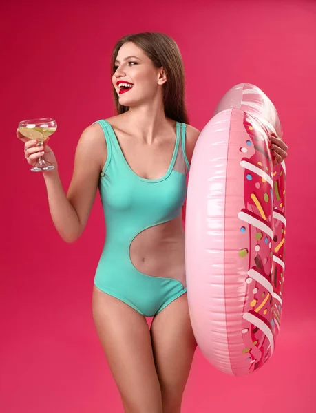Schöne junge Frau mit aufblasbarem Ring und Cocktail auf farbigem Hintergrund — Stockfoto