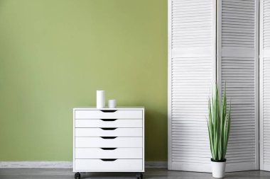 Çekmecelerin göğsü ve renkli duvara yakın katlanır ekran