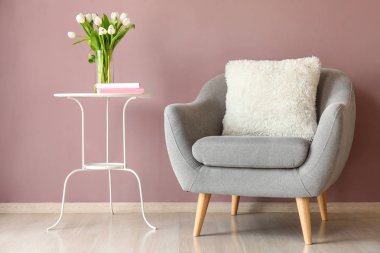 Odada renkli duvara yakın taze çiçekler ile rahat koltuk ve masa