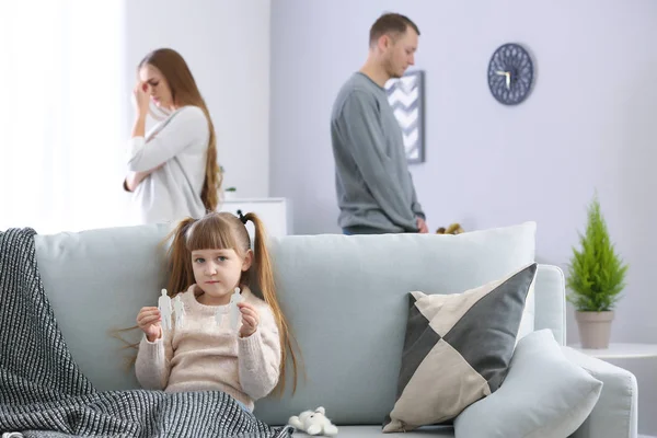 Sad little girl with broken figure of family sitting on sofa while her parents are arguing at home. Concept of divorce — Stock Photo, Image