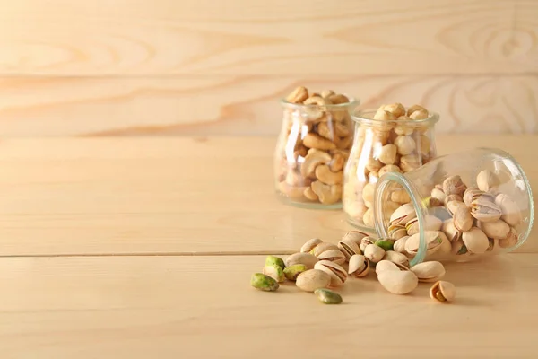 Frascos con diferentes frutos secos sabrosos en la mesa de madera — Foto de Stock