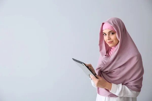 Mulher muçulmana jovem com computador tablet no fundo claro — Fotografia de Stock