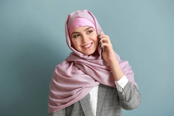 Beautiful Muslim woman talking by phone on color background — Stock Photo, Image
