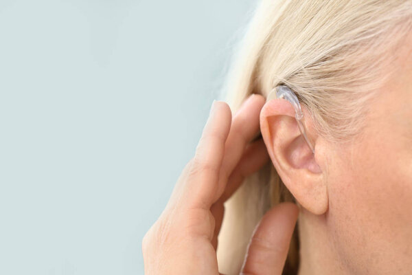 Зрелая женщина со слуховым аппаратом на светлом фоне, крупным планом
