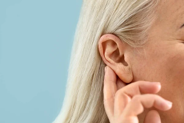 Oudere vrouw met gehoorprobleem op kleur achtergrond, close-up — Stockfoto