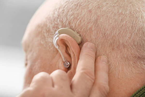 Старший мужчина со слуховым аппаратом дома, крупным планом
