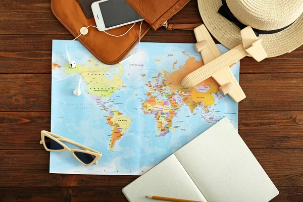 Mapa del mundo con avión, teléfono móvil y accesorios femeninos en mesa de madera. Concepto de viaje —  Fotos de Stock