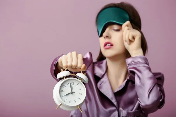 Sleepy woman with mask and alarm clock on color background