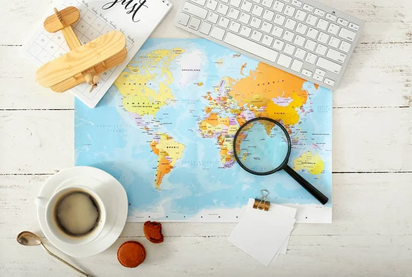 Mapa del mundo con avión, lupa, taza de café y teclado de la computadora en la mesa blanca. Concepto de viaje — Foto de Stock