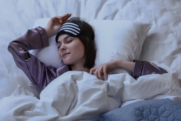 Giovane donna con maschera del sonno a letto di notte — Foto Stock